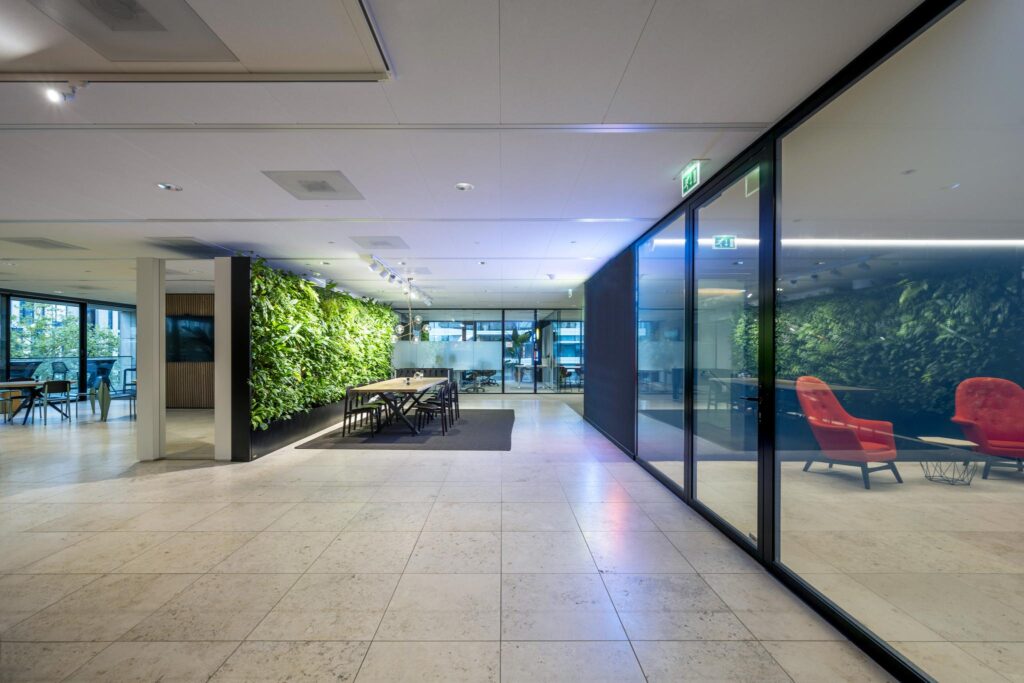 Modern office interior on Gustav Mahlerlaan with a green living wall, meeting table, and glass-walled lounge area.
